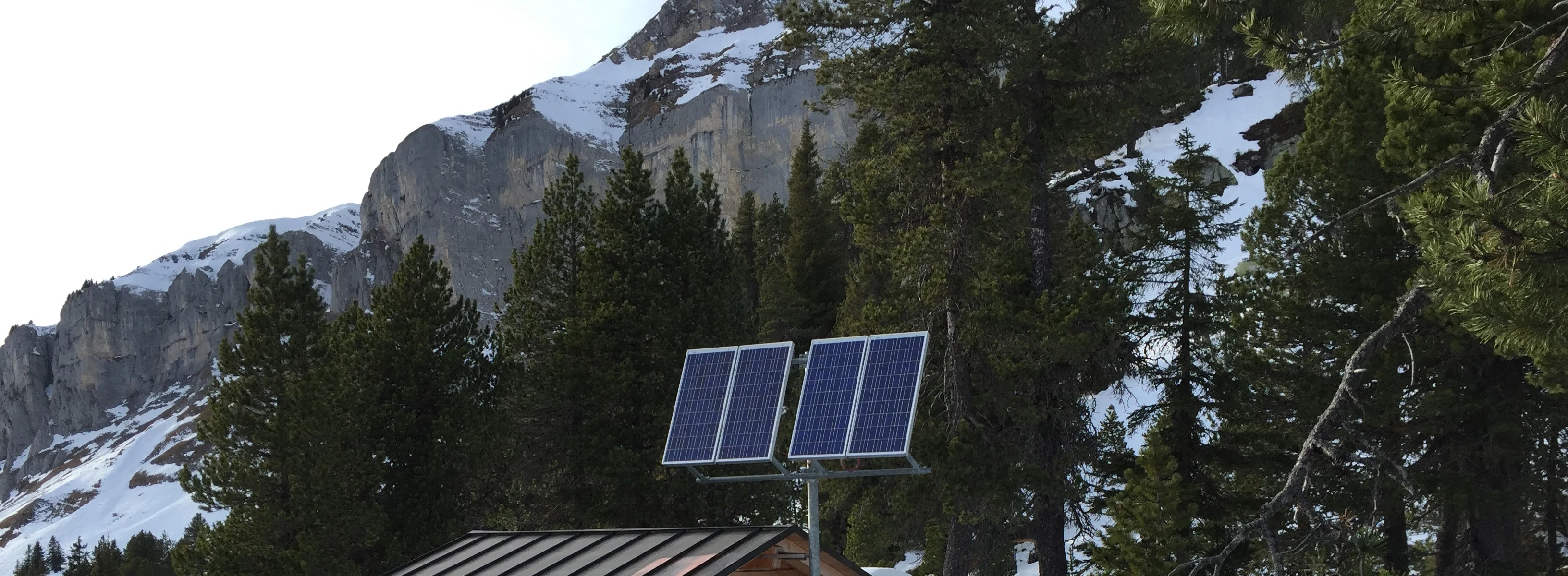 Photovoltaic modules above a mountain cabin in a snowy landscape